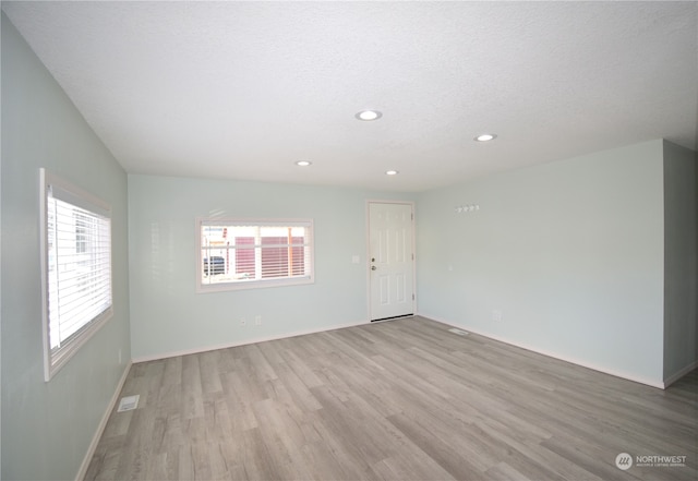 empty room with a textured ceiling and light hardwood / wood-style flooring