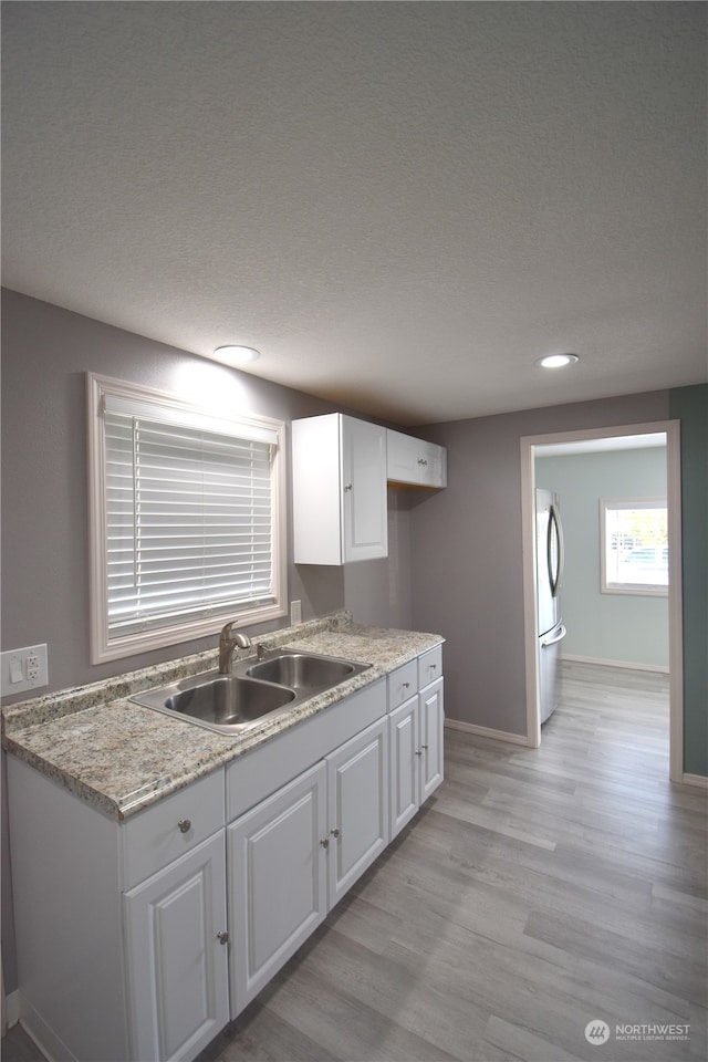 kitchen with stainless steel fridge, white cabinetry, a textured ceiling, light hardwood / wood-style flooring, and sink