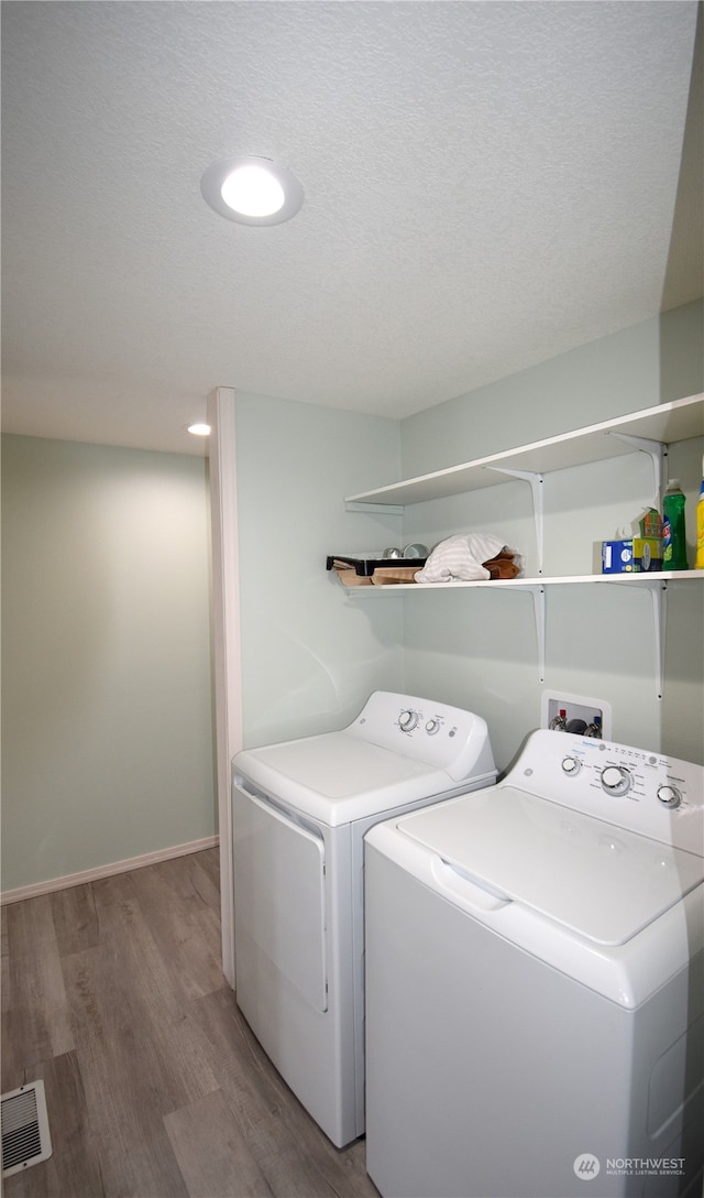 laundry area with light hardwood / wood-style floors, a textured ceiling, and washing machine and clothes dryer