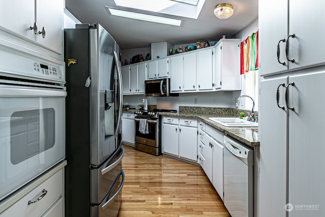 kitchen featuring appliances with stainless steel finishes, a skylight, sink, light wood-type flooring, and white cabinets