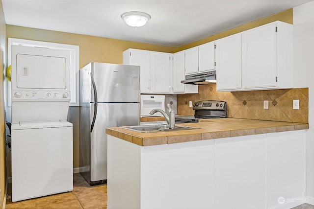 kitchen with stacked washer and dryer, appliances with stainless steel finishes, kitchen peninsula, and white cabinets