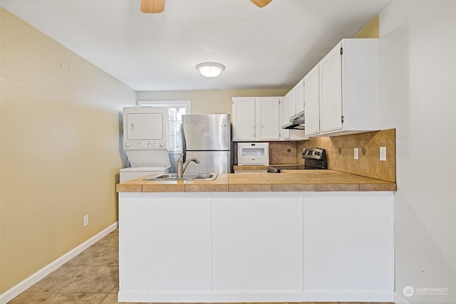 kitchen featuring kitchen peninsula, white cabinets, stacked washer / drying machine, sink, and stainless steel appliances