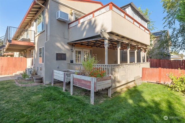 rear view of house with a wall unit AC, a yard, and a balcony