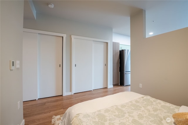 bedroom featuring light hardwood / wood-style flooring, stainless steel fridge, and multiple closets