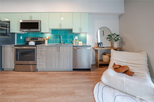 kitchen with decorative backsplash, appliances with stainless steel finishes, sink, light hardwood / wood-style floors, and green cabinetry