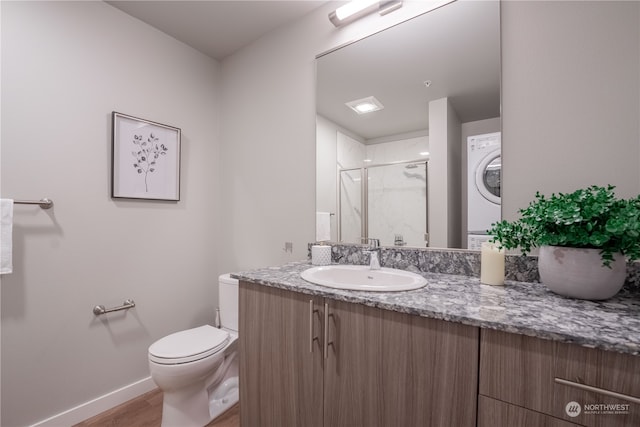 bathroom featuring stacked washer and clothes dryer, hardwood / wood-style flooring, toilet, a shower with shower door, and vanity