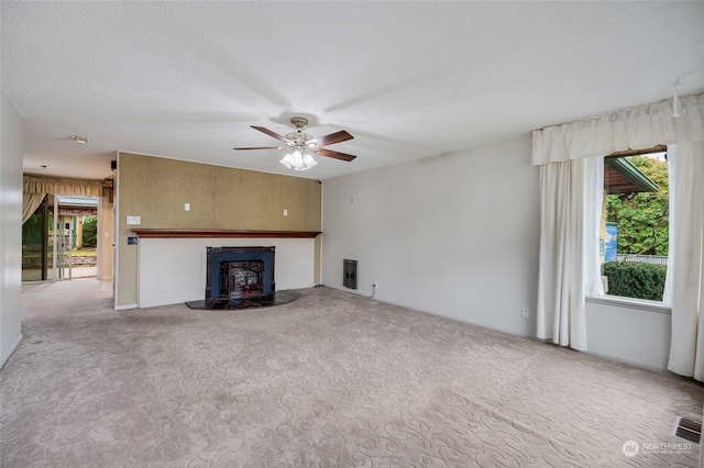 unfurnished living room featuring ceiling fan, a wood stove, a textured ceiling, and light colored carpet