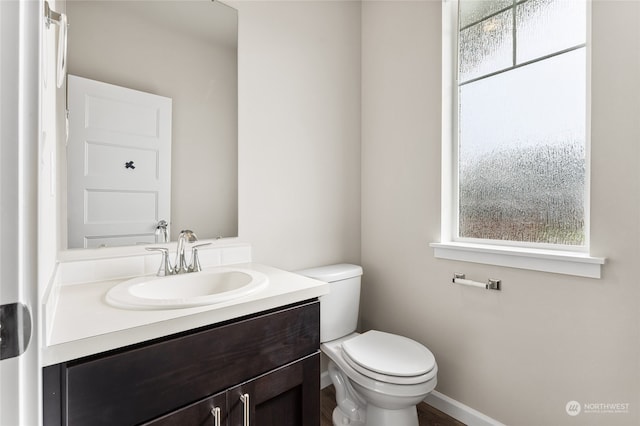 bathroom with a healthy amount of sunlight, toilet, vanity, and baseboards