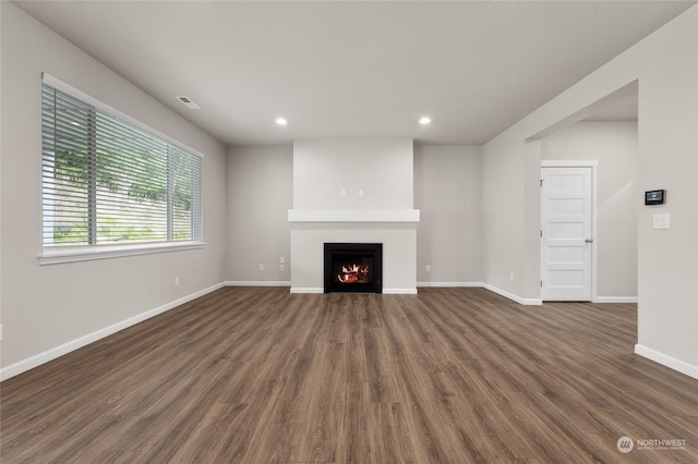 unfurnished living room with dark wood-type flooring, baseboards, visible vents, a warm lit fireplace, and recessed lighting