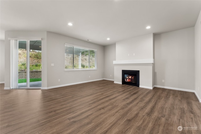 unfurnished living room featuring recessed lighting, baseboards, a glass covered fireplace, and dark wood-style flooring