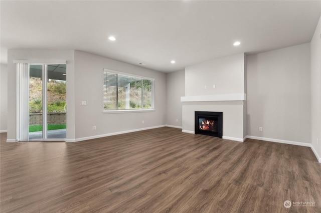 unfurnished living room featuring baseboards, a glass covered fireplace, recessed lighting, and dark wood-style floors