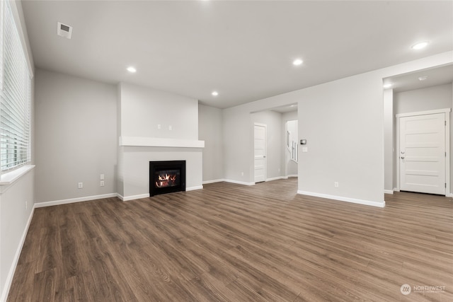 unfurnished living room with a glass covered fireplace, recessed lighting, wood finished floors, and visible vents