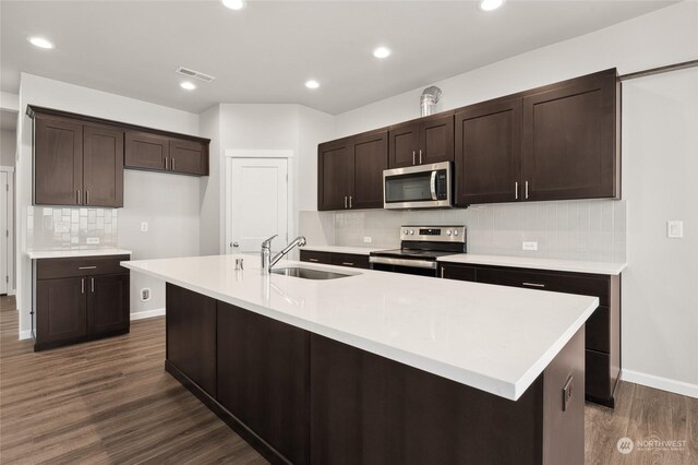 kitchen with dark wood finished floors, a sink, dark brown cabinetry, decorative backsplash, and appliances with stainless steel finishes