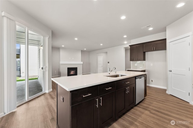 kitchen featuring dishwasher, light wood finished floors, a sink, a lit fireplace, and a kitchen island with sink