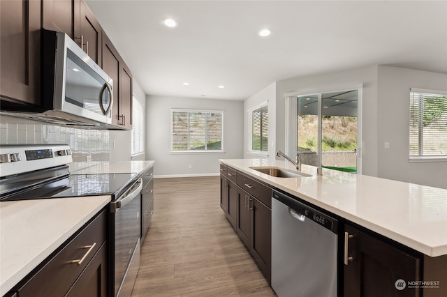 kitchen featuring light wood finished floors, dark brown cabinetry, light countertops, appliances with stainless steel finishes, and a sink