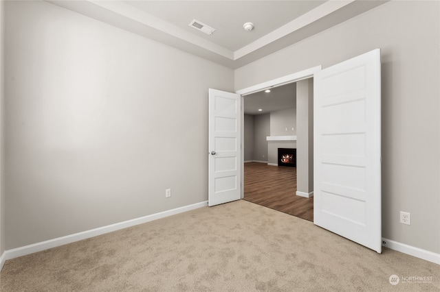 empty room with a warm lit fireplace, baseboards, visible vents, and carpet floors