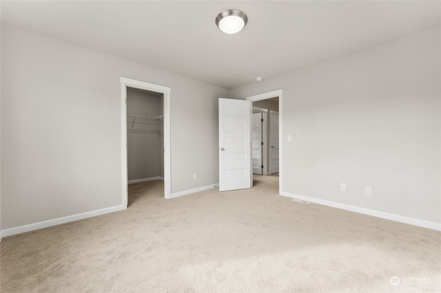 unfurnished bedroom with a closet, light colored carpet, a walk in closet, and baseboards