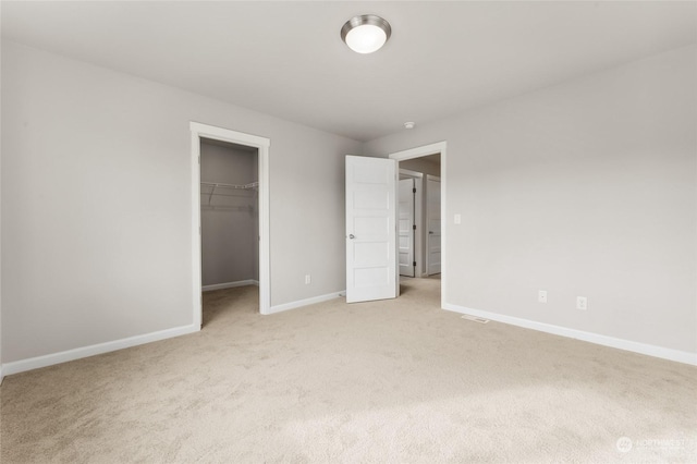 unfurnished bedroom with a closet, light carpet, baseboards, and a spacious closet