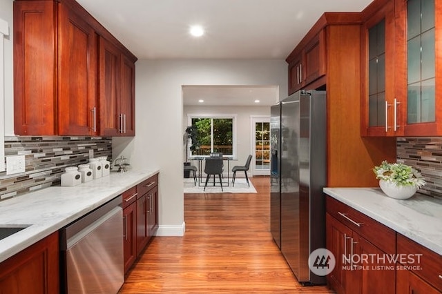 kitchen with light stone countertops, light hardwood / wood-style floors, stainless steel appliances, and decorative backsplash