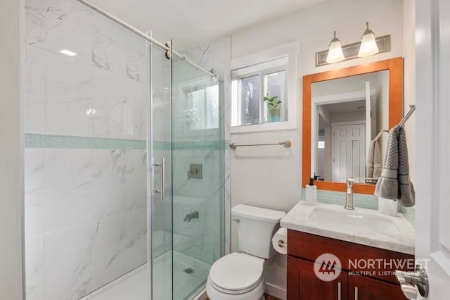 bathroom featuring a shower with door, vanity, and toilet