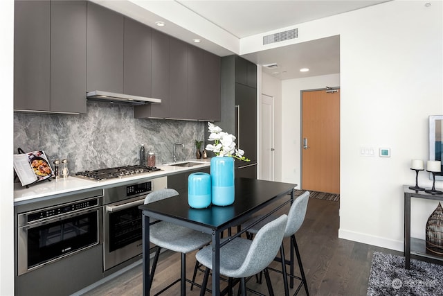 kitchen with gray cabinetry, backsplash, stainless steel appliances, dark wood-type flooring, and ventilation hood