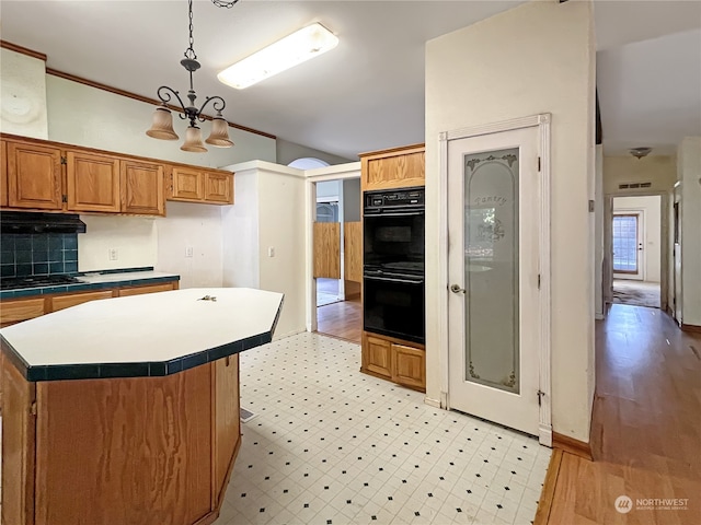 kitchen with a kitchen island, pendant lighting, light wood-type flooring, black double oven, and tasteful backsplash