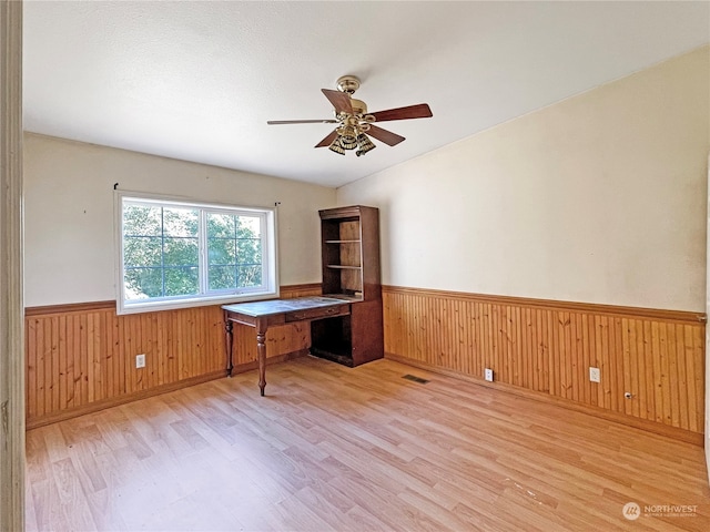 unfurnished office with lofted ceiling, wooden walls, light hardwood / wood-style floors, and ceiling fan