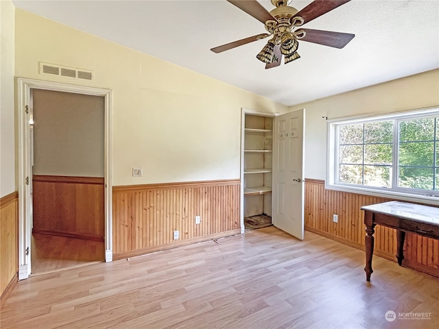 unfurnished office with light hardwood / wood-style floors, wood walls, vaulted ceiling, and ceiling fan