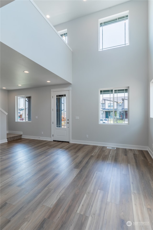 unfurnished living room with a wealth of natural light, a towering ceiling, and wood-type flooring