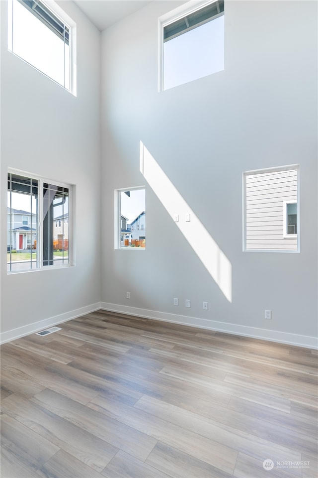 unfurnished living room with plenty of natural light, light hardwood / wood-style floors, and a high ceiling