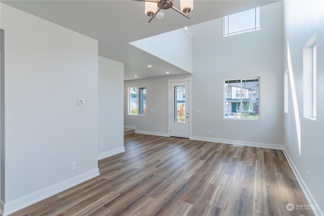 unfurnished living room with a notable chandelier, wood-type flooring, and a towering ceiling