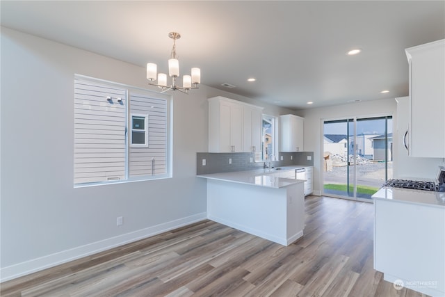 kitchen featuring pendant lighting, white cabinets, sink, light wood-type flooring, and kitchen peninsula