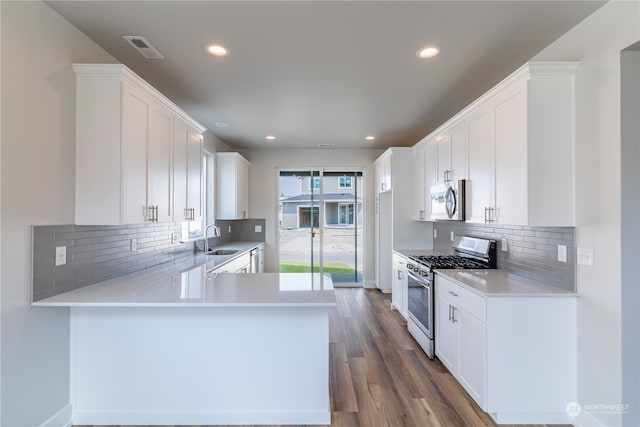 kitchen with stainless steel appliances, tasteful backsplash, dark hardwood / wood-style flooring, kitchen peninsula, and white cabinets