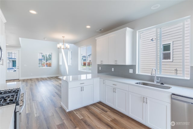 kitchen with hardwood / wood-style floors, kitchen peninsula, sink, appliances with stainless steel finishes, and white cabinetry