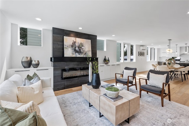 living room featuring an AC wall unit, light wood-type flooring, and a tile fireplace