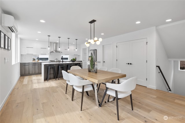 dining space with sink, light wood-type flooring, and a wall unit AC