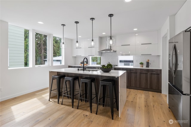 kitchen with sink, stainless steel fridge, wall chimney exhaust hood, pendant lighting, and white cabinets