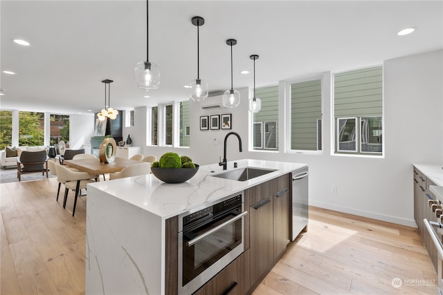 kitchen featuring a center island with sink, light wood-type flooring, stainless steel appliances, sink, and light stone counters