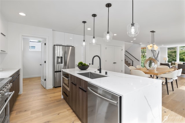 kitchen with appliances with stainless steel finishes, sink, light wood-type flooring, an island with sink, and decorative light fixtures