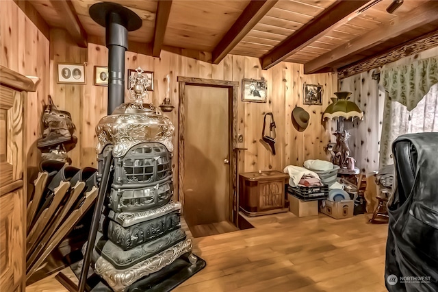 interior space with wood walls, wood ceiling, a wood stove, hardwood / wood-style floors, and beam ceiling