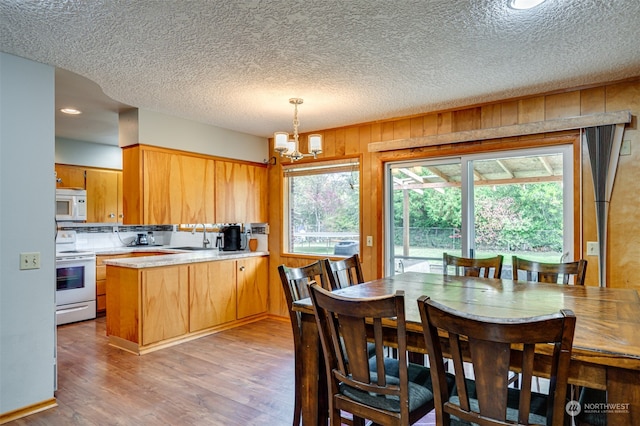 kitchen with wooden walls, kitchen peninsula, white appliances, pendant lighting, and light hardwood / wood-style floors