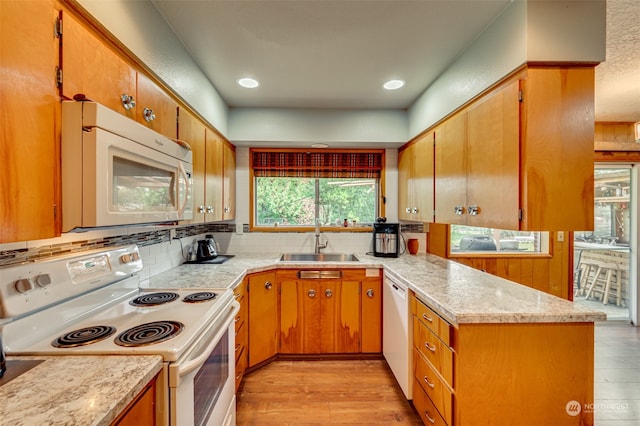 kitchen featuring kitchen peninsula, backsplash, light wood-type flooring, sink, and white appliances