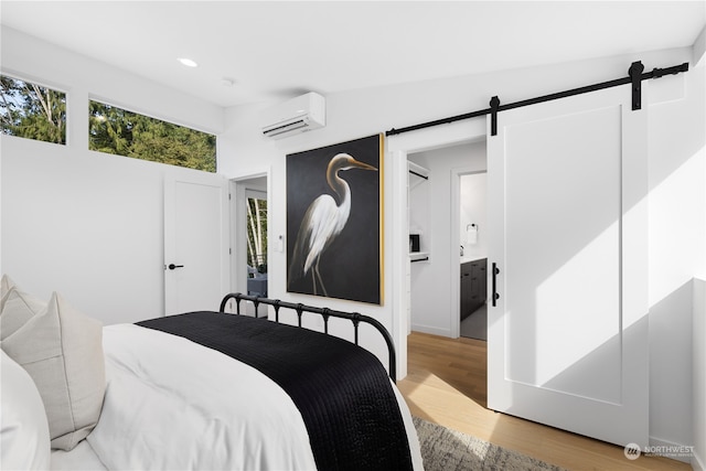 bedroom with ensuite bath, a wall unit AC, a barn door, hardwood / wood-style floors, and lofted ceiling