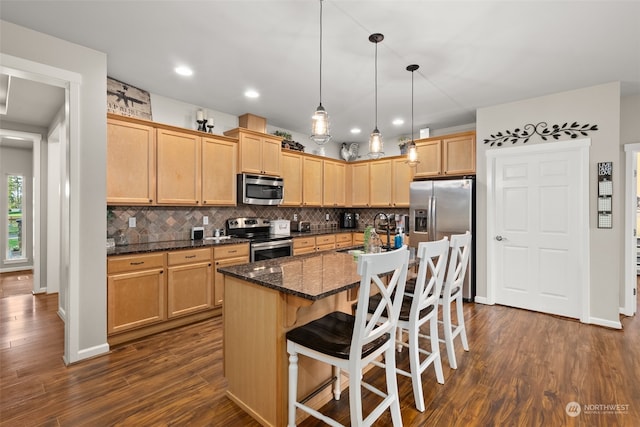 kitchen featuring dark hardwood / wood-style flooring, appliances with stainless steel finishes, a kitchen breakfast bar, a kitchen island, and dark stone countertops