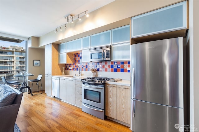 kitchen featuring sink, backsplash, light hardwood / wood-style flooring, and appliances with stainless steel finishes