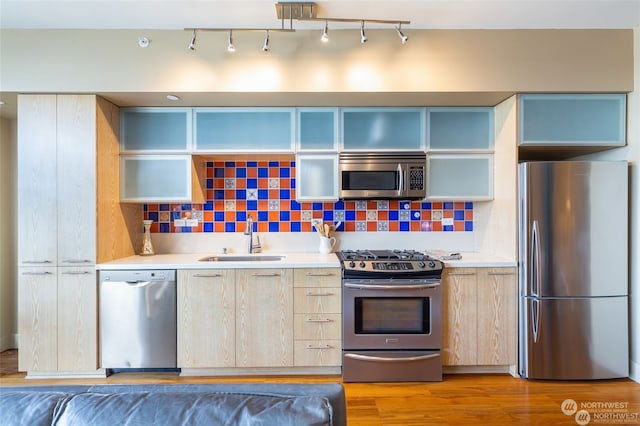 kitchen with sink, hardwood / wood-style flooring, appliances with stainless steel finishes, backsplash, and light brown cabinets