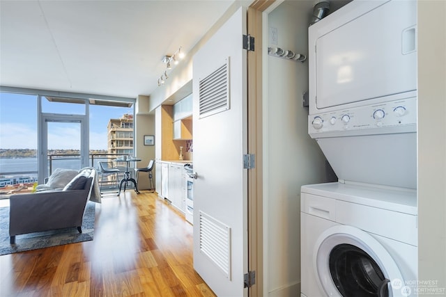 clothes washing area with a water view, rail lighting, stacked washer and clothes dryer, and light hardwood / wood-style flooring