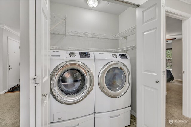 laundry area with crown molding, washing machine and dryer, and light colored carpet