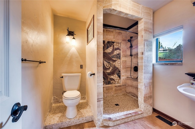 bathroom featuring a tile shower, wood-type flooring, and toilet