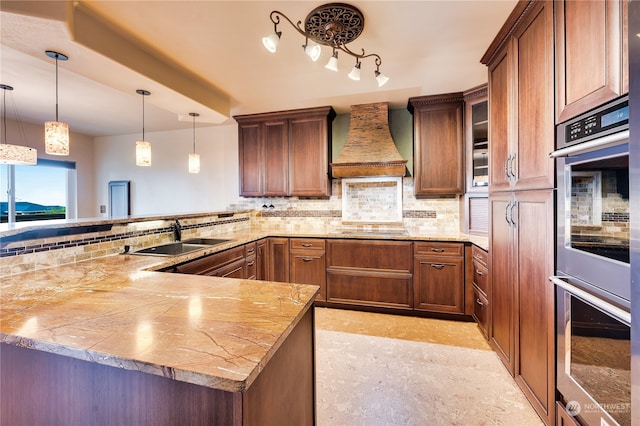 kitchen featuring kitchen peninsula, hanging light fixtures, custom range hood, double oven, and sink